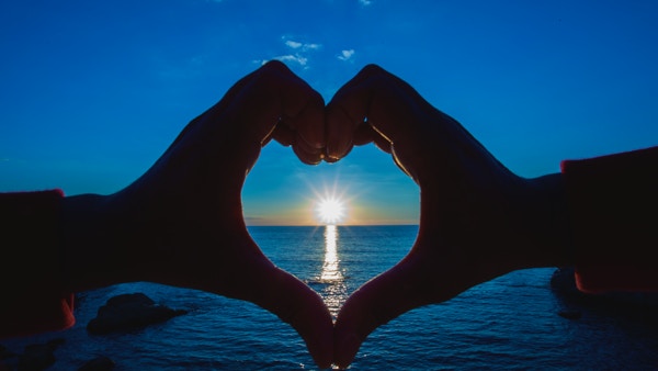 Hjerteform laget med hender som omslutter den kypriotiske morgensolen i horisonten.