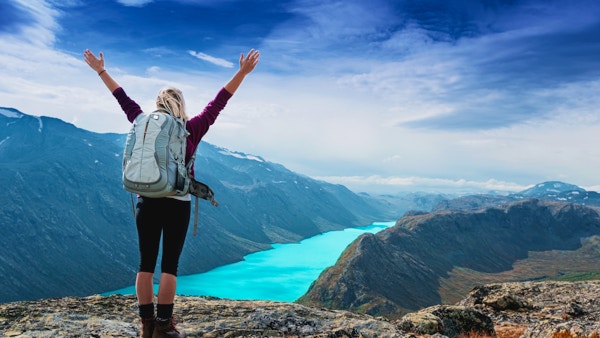 Ung turistkvinne som føler seg fri og står med hendene i været på toppen av fjellstien mens hun ser på et vakkert landskap