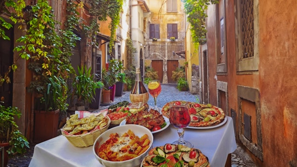 Bord med italienske retter som pasta og pizza i en idyllisk bakgate i Roma.