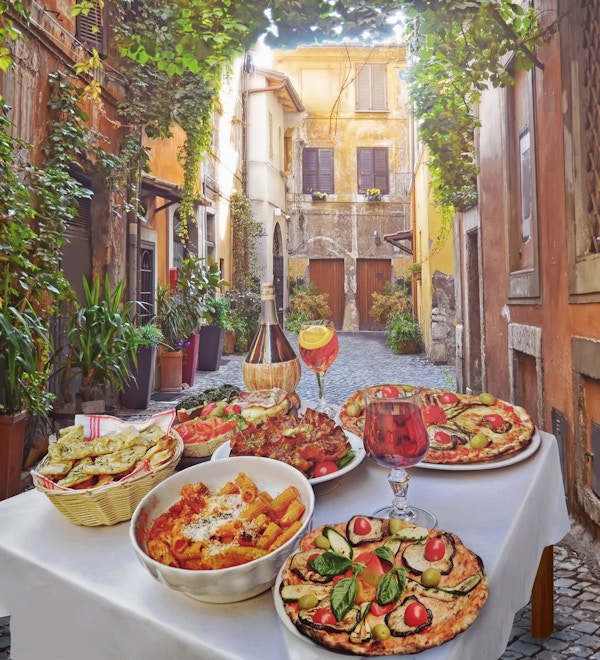 Bord med italienske retter som pasta og pizza i en idyllisk bakgate i Roma.