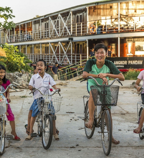 Smilende barn på sykler foran et elvecruiseskip i Vietnam. Foto.