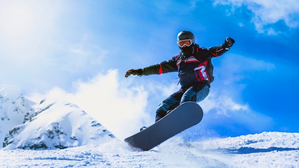 Mann som hopper med snowboard fra fjellbakken