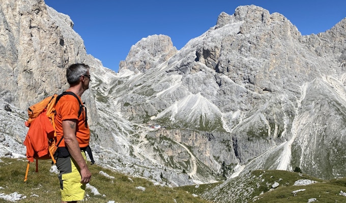 Mann med ryggsekk som ser utover dal og mot høye fjell