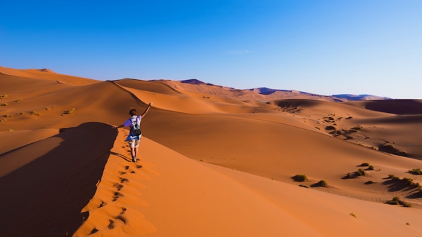 Turist som går på de naturskjønne sanddynene i Sossusvlei, Namib-ørkenen, Namib Naukluft nasjonalpark, Namibia. Ettermiddagslys. Eventyr og utforsking i Afrika.