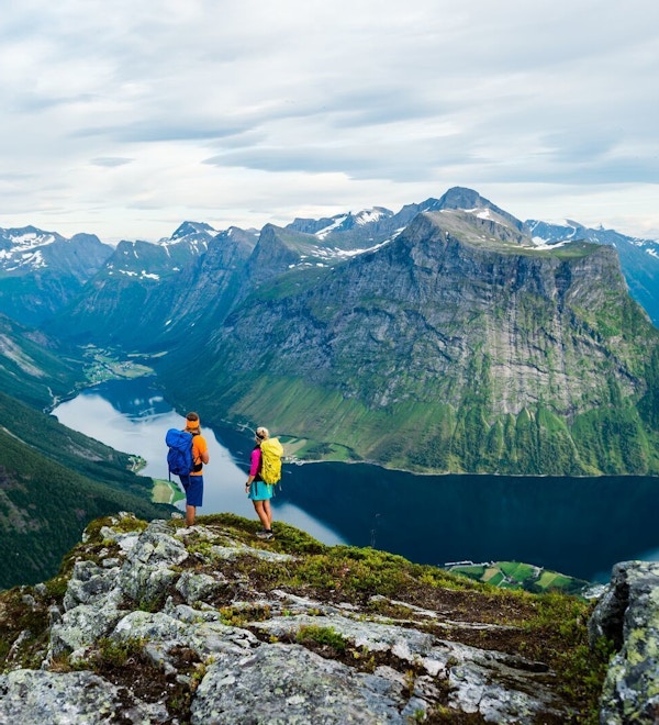 2 mennesker med turklør og tursekk på ryggem på toppen av fjellet og ser ut over Hjørundfjorden