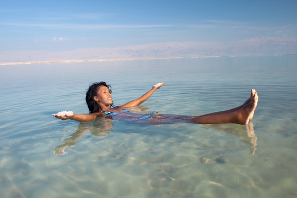 Ung kvinne som flyter på ryggen i Dødehavet, og holder mineralsalt i begge hender. Den uvanlige oppdrift forårsaket av høy saltholdighet.