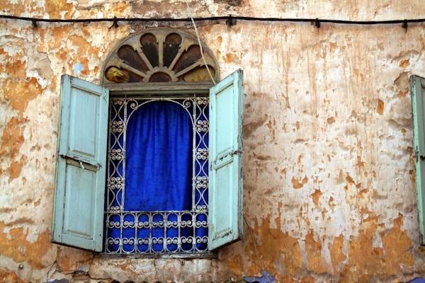 En blått vindu på en vegg med gammel maling