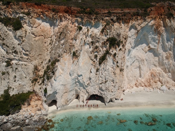 En hvit strand med turister som soler seg ved det grønne havet foran en høy klippe