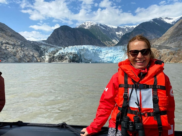 Kvinne med redningsvest i båt med isbre i bakgrunnen
