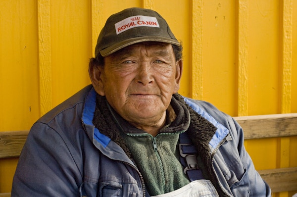 En gammel mann som sitter på en benk foran en gul husvegg