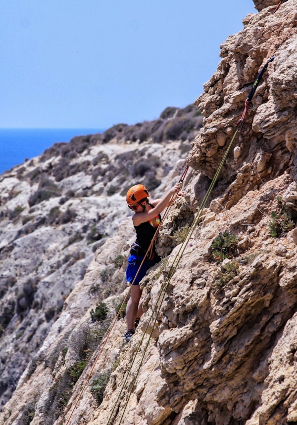 En jente klatrer i tau i fjellveggen på Malta