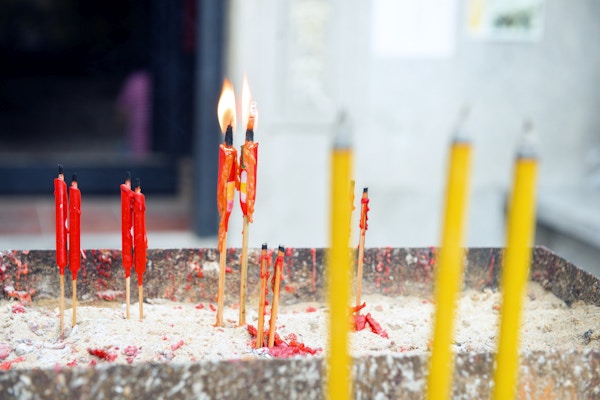 Dette er et horisontalt fargefotografi av røde lys som brenner og er plassert utenfor et buddhisttempel.