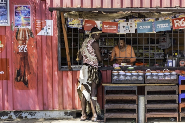 Johannesburg, Sør-Afrika - 24. september 2013: Afrikansk zulu-mann kledd i sin tradisjonelle klær, handlet på en spaza-butikk i Orlando, Soweto. Butikken er laget av en gammel fraktbeholder med skilt og plakater festet på seg. Den er innbruddssikker for sikkerhets skyld.