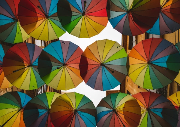 Mange fargerike paraplyer henger høyt over ei gate i en by
