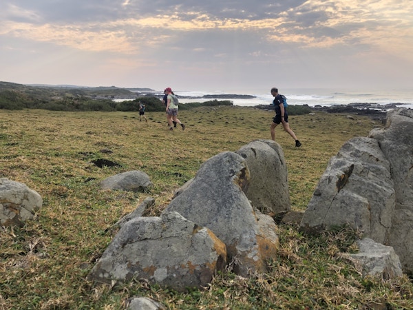Fire personer vandrer langs kysten der det ligger store steiner langs stien