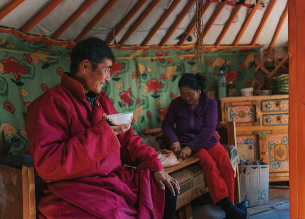 Mongolsk mann nyter geitemelkete inne i yurt sammen med familien