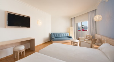 Hotellrom med to senger, liten sofa og tv med en liten benk under