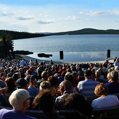 Panoramabilde av publikum sett bakfra med scenen på Peer Gynt spelet foran Gålåvatnet i bakgrunnen