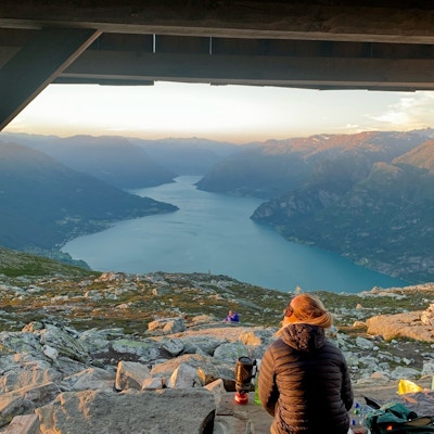 Jente sitter med ryggen til kamera og ser på utsikten over sognefjorden i solnedgang i sherpahytta på toppen av fjellet Molden