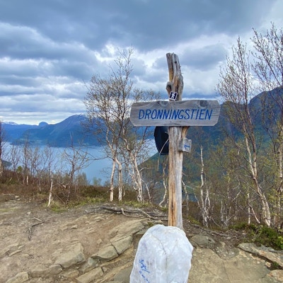 Skilt ved startpunktet til Dronningstien med utsikt over Hardangerfjorden og en stein signert av Dronning Sonja