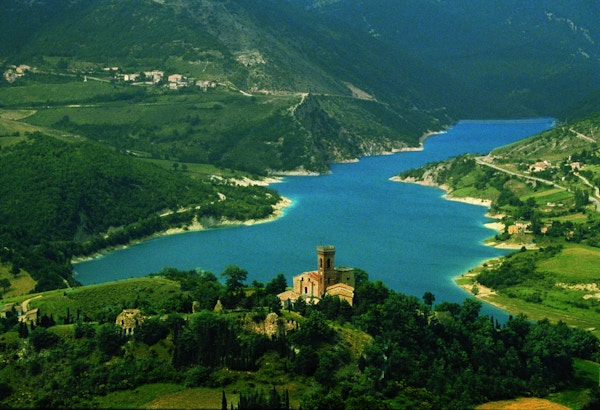 Bilde tatt fra topp med utsikt over innsjøen Fiastra samt slott og bebyggelse rundt innsjøen og skogkledde åser