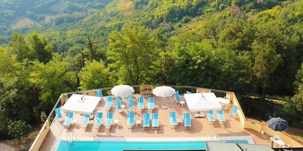 Svømmebassenget, solsengene og parasollene på Hotel Centopini sett ovenfra med trær i bakgrunnen