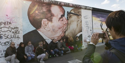 En gruppe mennesker poserer foran berlinmuren og broderkysset mens de blir tatt bilde av