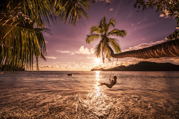Ung, glad kvinne som gleder seg i en vakker solnedgang på stranden mens hun svinger over vannet.