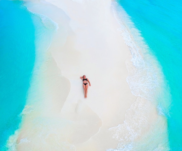 Vakker kvinne som ligger på sandbanken omgitt av turkis hav ovenfra