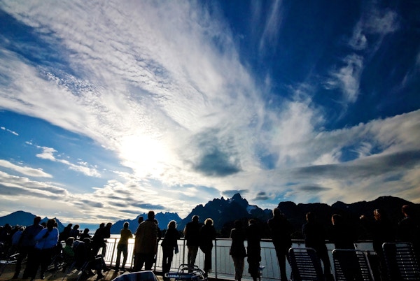 Mennesker står og ser utover relingen på skip mot fjell og fjord