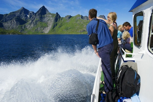 To mennesker ser utover landskapet fra båten som kjører på vannet mot fjellene i bakgrunnen