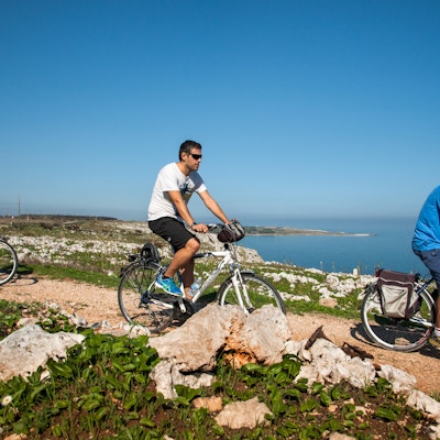 Tre personer sykler på grussti langs kysten i Puglia