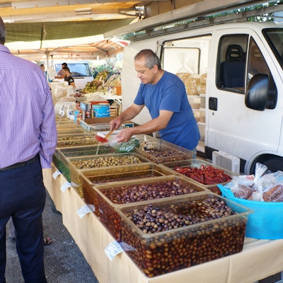 En markedsbod med mange forskjellige typer oliven i bakker, en mann kjøper fra selgeren