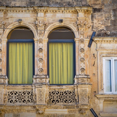 Et vindu i et gammelt bygg i Lecce, omringet av flotte detaljer på fasaden