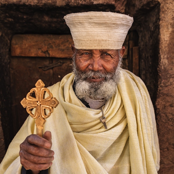 Katolsk prest som står foran en av steinhugges kirker i Lalibela. Etiopia, Øst-Afrika