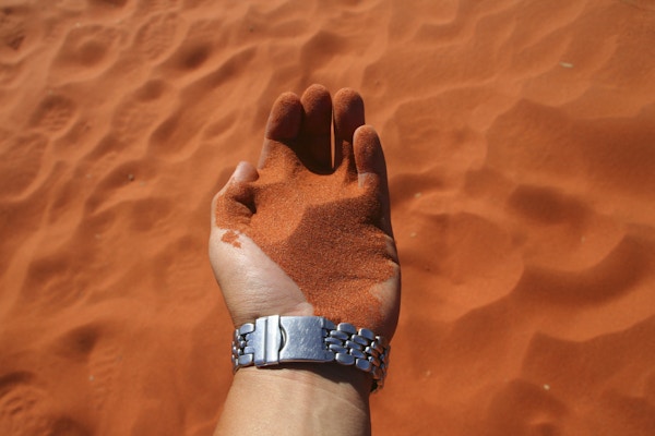 En person holder oransje ørkensand i hånden sin