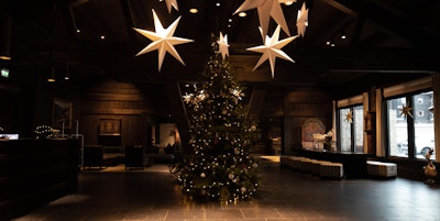 Stort juletre pyntet med gullfargede julekuler og stor stjerne i toppen. Stjerner hengende fra taket også