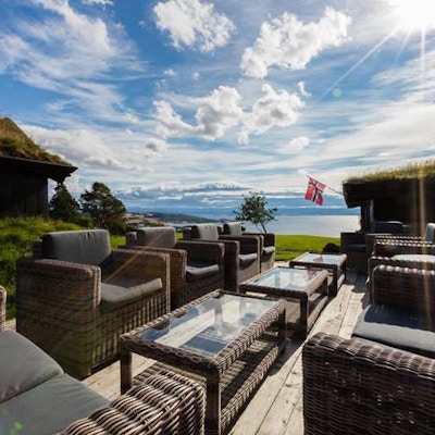 Hagemøbler ute på en terrasse med utsikt over fjord og fjell. Norsk flagg vaier