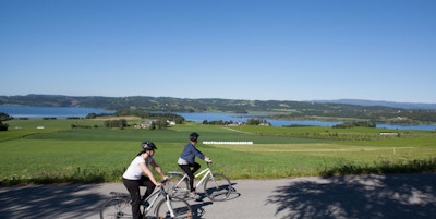 to syklister ute på tur med hjelm og fritidsklær. Utsikt over grønne sletter og vann