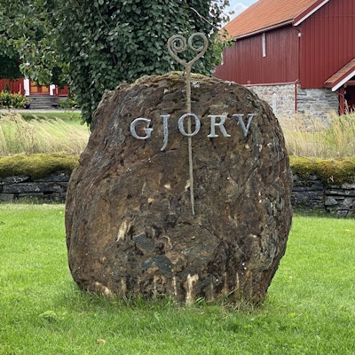 Gammel stein med mose ønsker velkommen til Gjørv Gård. Rød låve i bakgrunnen