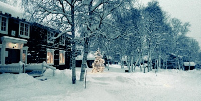 Bjørketrær i snøen omkranser tradisjonell trebygning med rekkverk og veranda