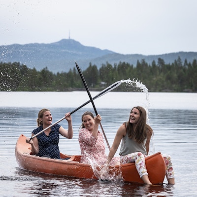 tre jenter ute i kano som spruter med åre og har det gøy