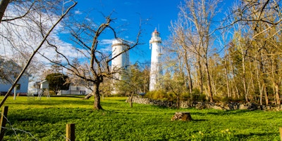 Avstandsbilde av to hvite fyrtårn med trær i forgrunnen og grønt gress