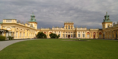 Et stort slott bygget i halvsirkel med gul fasade og stor park tilknyttet
