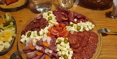Tallerken og kurv med ost, skinke, pølser, brød og salat på et bord