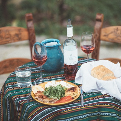 Tradisjonell gresk matrett med tilhørende brød og en flaske vin, plassert på et bord utendørs