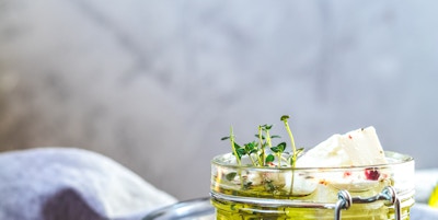 Fetaost marinert i olivenolje med friske urter i glasskrukke. Trebakgrunn.