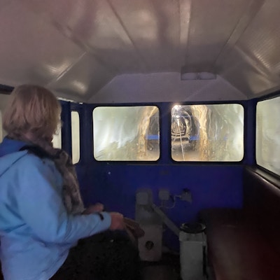 Kvinne i blå jakke sett fra siden sitter i vogn i fjellbane