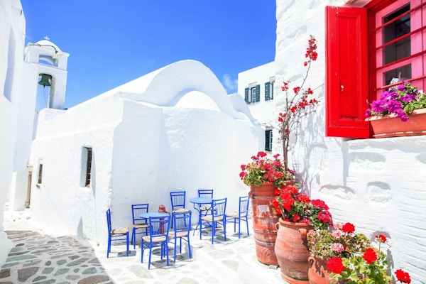Hvite bygninger, blå stoler og bord samt krukker med rød blomster