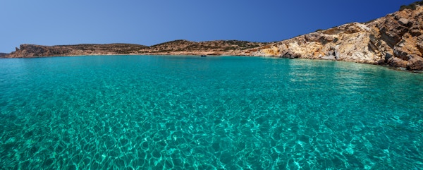 Gjennomsiktig vann og en liten forankret trebåt, på øya Kato Koufonissi, Kykladene, Hellas.